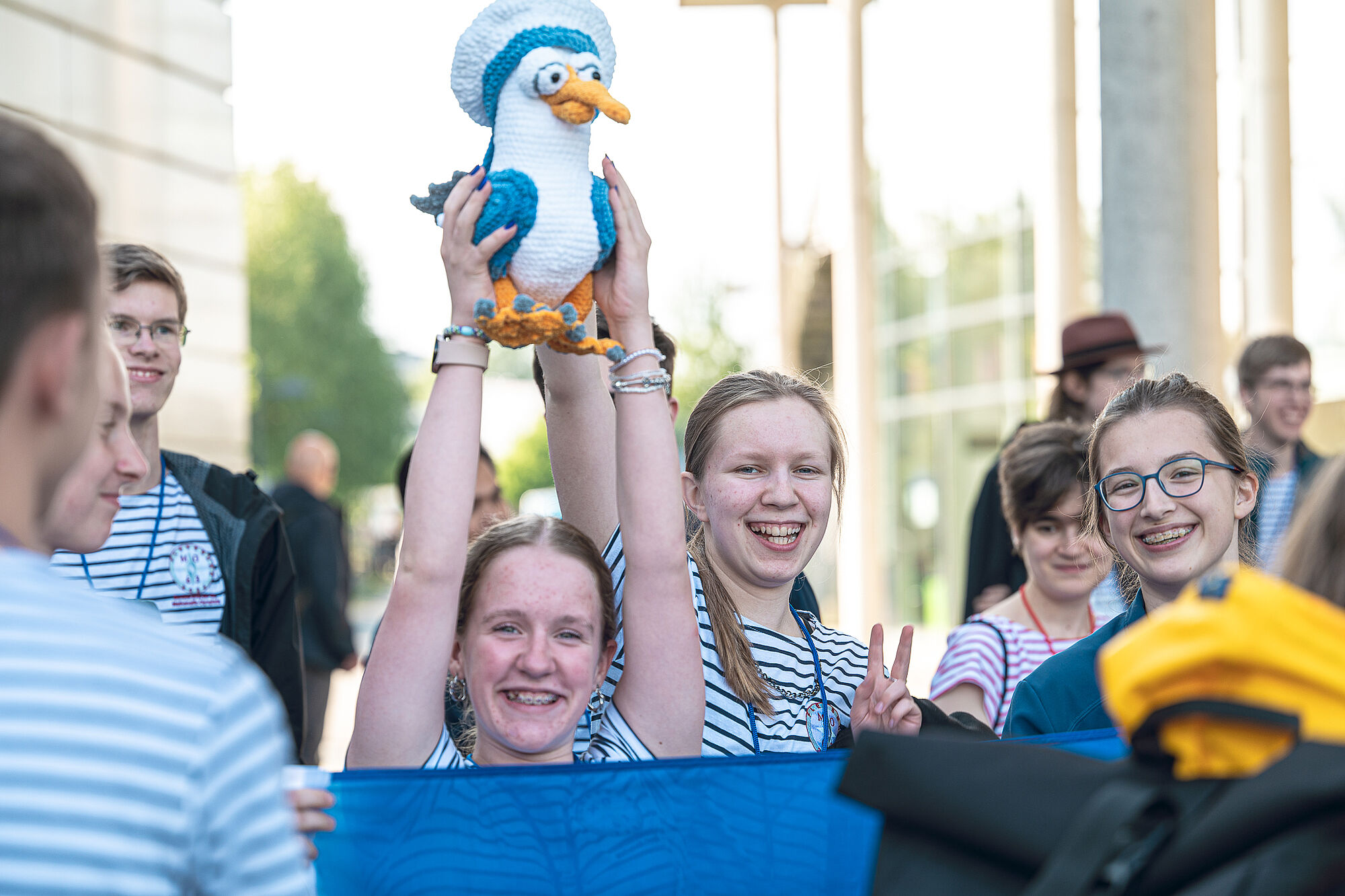 Teilnehmerinnen der MO-Bundesrunde 2024 lachen in die Kamera; ein Mädchen in der Mitte reckt eine gehäkelte Möwe in die Höhe. 